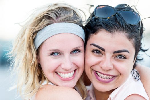 Two smiling young women posing together, one caucasian and one hispanic or middle eastern